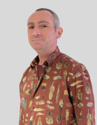 Leitender Oberarzt Krohmer ohne Kittel mit braun-bunt-bedrucktem Hemd, kurzen grauen Haaren und einem leichten Lächeln, nach vorne gerichtet